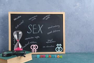 Chalkboard with written text,  hourglass, book and eyeglasses on table. Sex education