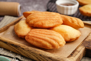 Wooden board with delicious madeleines on grey background, closeup