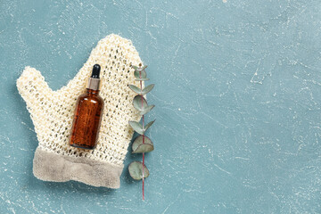 Bottle of essential oil, massage glove and eucalyptus branch on color background