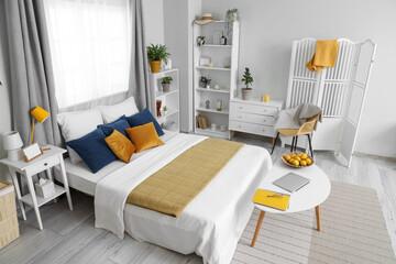 Modern interior of bedroom with comfortable bed, chair, shelving units and bedside tables