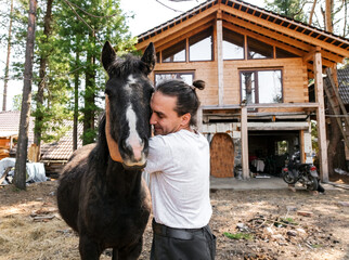 rustic man with  horse in rural village near  forest.  horse farm is surrounded by nature, hay is stacked nearby,  peaceful and traditional.  man is caring for  horse