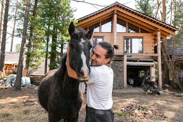 rustic man with  horse in rural village near  forest.  horse farm is surrounded by nature, hay is stacked nearby,  peaceful and traditional.  man is caring for  horse
