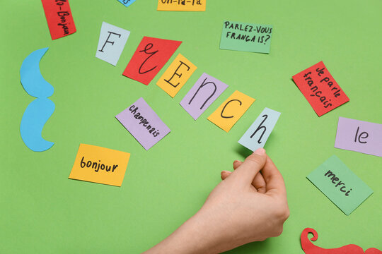 Female hand and paper sheets with French words on green background, closeup