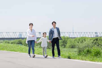 手を繋いで土手を歩く家族