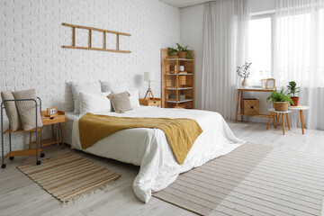 Stylish interior of bedroom with big comfortable bed and stepladder on white brick wall