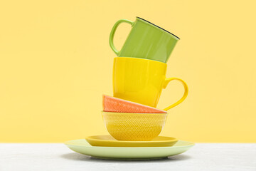 Set of clean plates and cups on table against yellow background
