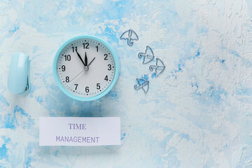 Paper with text TIME MANAGEMENT, alarm clock and stapler on blue grunge background. Top view