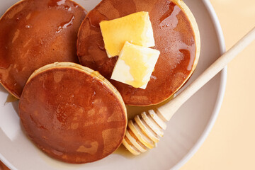 Tasty pancakes with honey and butter on orange background