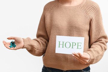 Young woman holding teal ribbon and paper with word HOPE on white background, closeup. Sexual...