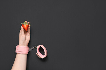 Female hand in handcuffs with fresh strawberry on black background. Sex education