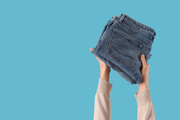 Female hands with stack of stylish jeans on blue background, closeup