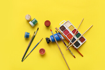 Artist brushes and paints on yellow background