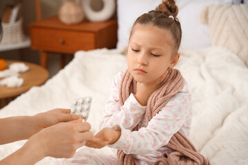 Fototapeta premium Sick little girl with sore throat taking pills from mother in bedroom