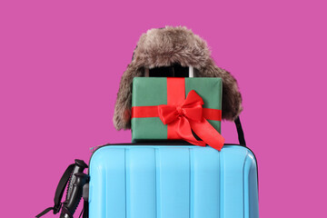 Suitcases with gift box and winter hat on purple background. Closeup