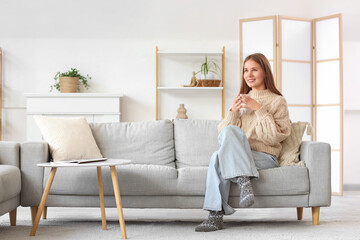 Young woman with cup of tea sitting on sofa at home