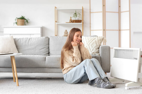 Young woman sitting near electric convector heater at home