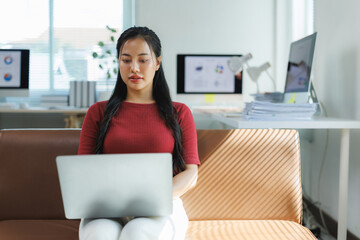 Asian freelancer working from home using laptop on sofa