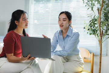 Two young businesswomen discussing work on laptop in modern office
