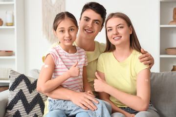 Family with medical patches after vaccination showing thumbs-up on sofa at home