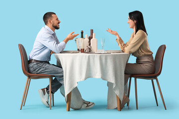 Young couple talking at restaurant table on blue background