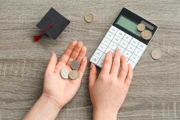 Woman with coins using calculator on wooden table. Student loan concept