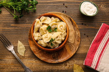 Bowl of delicious boiled dumplings with parsley and sour cream on wooden background