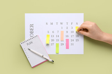 Female hand with notebook and sticky notes marking dates in calendar on green background. Planning...
