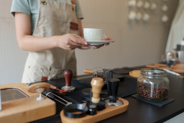 Barista holding cup of coffee over counter with equipment and coffee beans
