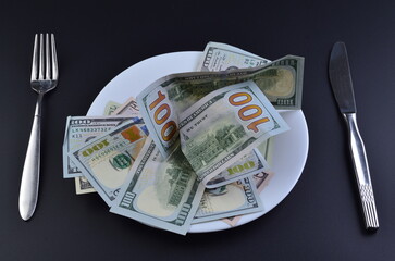 Crumpled dollar bills on plate with cutlery on black background