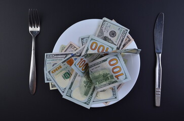 Crumpled US dollar bills served on white plate with fork and knife