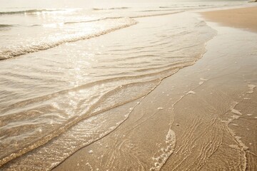 Gentle Ocean Waves Washing Over Sandy Beach. Peaceful shoreline with soft waves lapping against the golden sand, captured in warm sunlight during a calm day at the beach