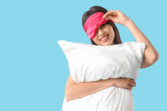 Young woman in sleeping mask with pillow on blue background