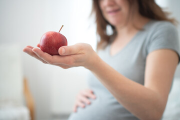 Close-up of pregnant woman holding apple while lovingly stroking her rounded belly. Nourishing...