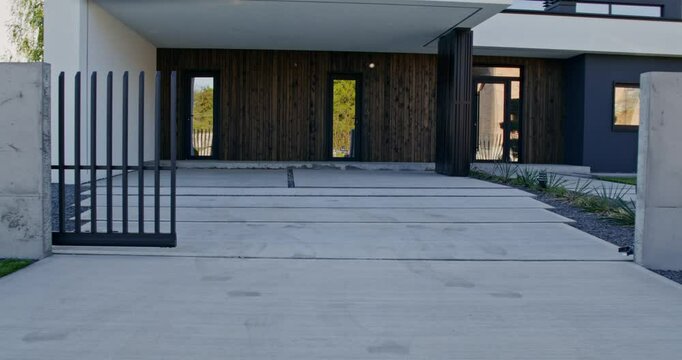 The facade of a stylish minimalist modern cottage with a well-kept house territory on a summer day. Automatic gate closing