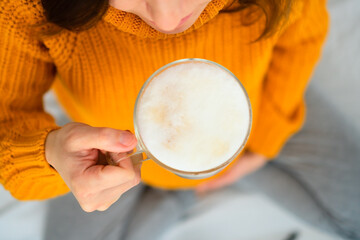 Aerial close-up of pregnant woman enjoying latte in meditation pose, reflecting on dietary guidelines. Warm atmosphere of conscious enjoyment.