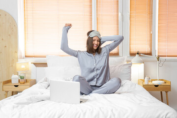 Happy young woman with laptop sitting in bedroom