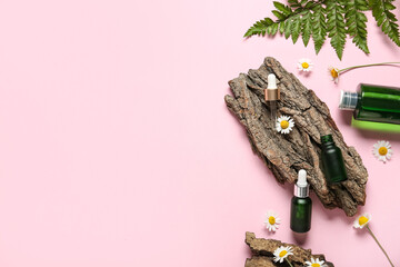 Bottles of cosmetic products, chamomile flowers and tree bark on pink background