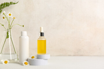 Chamomile flowers, plaster podiums and bottles of cosmetic products on table near beige wall