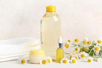 Chamomile flowers, towels, bottles and jar of cosmetic products on table near beige background, closeup