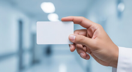 Close-up View of a Hand Holding a Blank White Card in a Medical Setting with Blurred Background