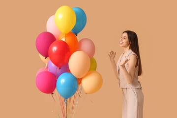 Happy young woman with colorful air balloons on beige background