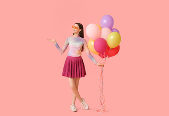 Happy young woman in sunglasses with colorful air balloons on pink background