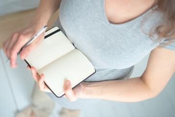 Overhead shot of future mother writing crucial to-do list for maternity period. Detailed...