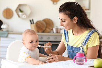 Young mother feeding her baby in high chair at home