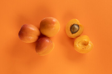 A minimalist flat lay of whole and halved apricots arranged on a vivid orange backdrop. 