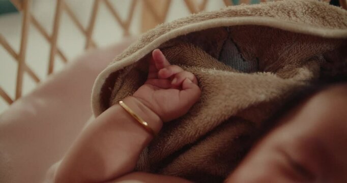 Newborn baby infant arm hand cute close up while resting in a wooden cradle box in warm natural light wearing golden bracelet