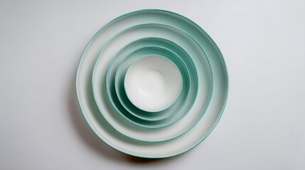 Four white ceramic bowls with teal rims nested inside each other on a light background.