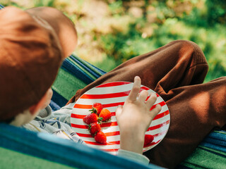 Young Boy in Cap Eating Strawberry in Hammock