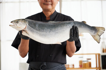 close up chef holding and showing a big raw salmon in the kitchen