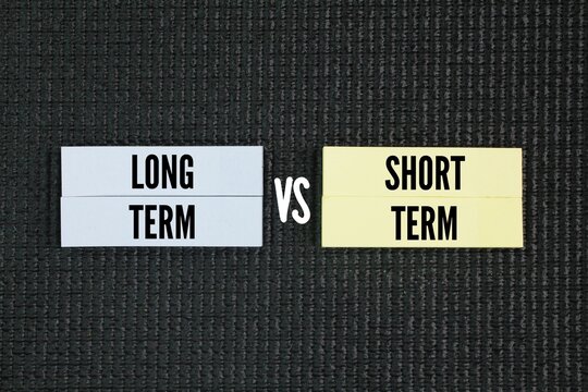 Colored paper with the words long term vs short term. Short-term goals are likely measured by weeks, months, or quarters. Long-term goals can be measured by years and may have an undefined timeline